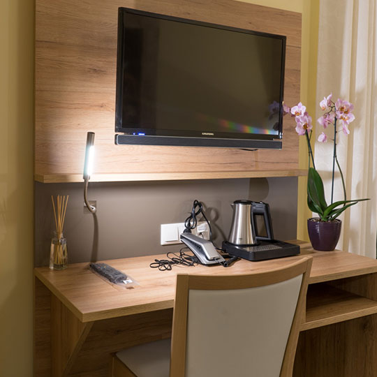 Schreibtisch mit Wand-TV, Leselampe, Telefon, Wasserkocher auf Tablett und rosa Blütenorchidee
