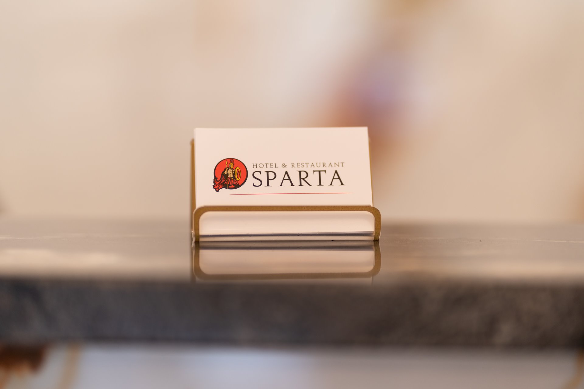 Visitenkarte von Hotel & Restaurant Sparta mit spartanischem Helm-Logo in edlem Metallhalter auf Tresen