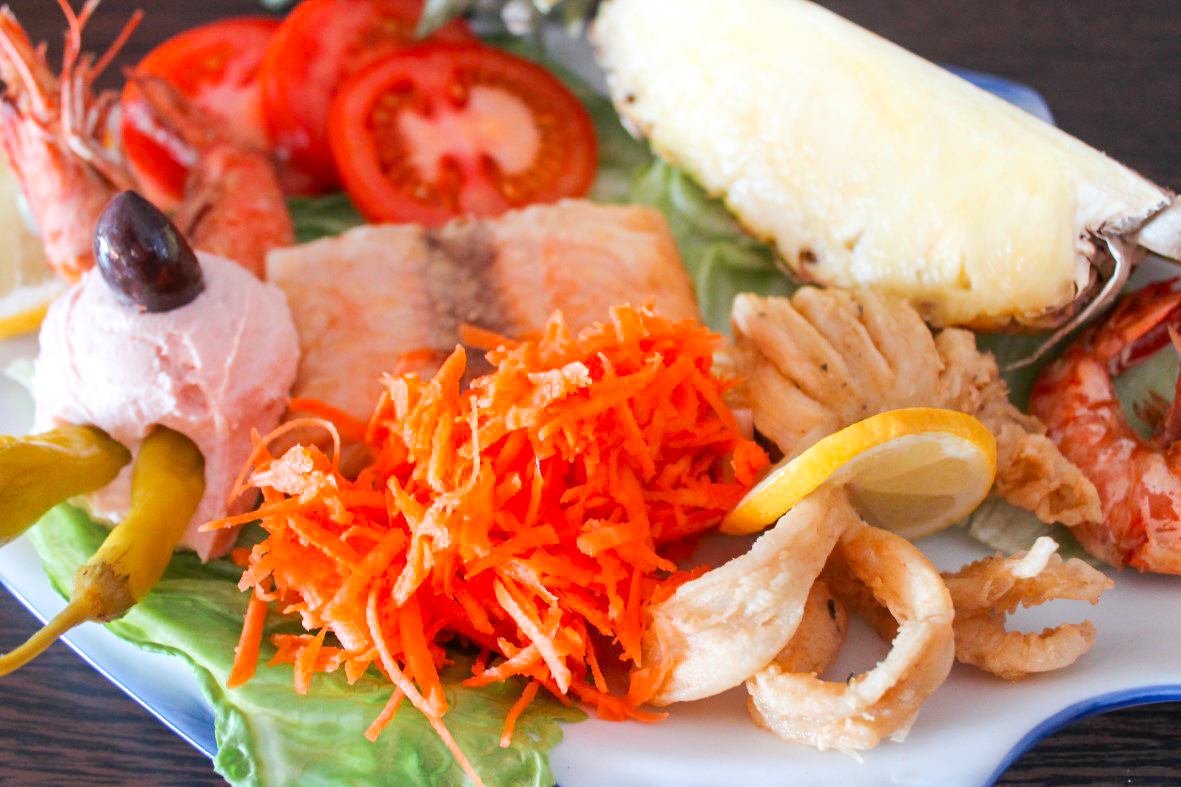Gemischte Meeresfrüchteplatte mit Garnelen, Räucherfisch, frittierten Calamariringen, Karottensalat, Tomatenscheiben, Frischkäse mit Olive und Ananasspalte