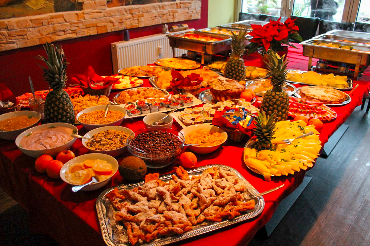 Frühstücksbuffet mit Müsli, Joghurt, Obst- und Käseplatten, Ananas und süßem Gebäck auf rotem Tischtuch