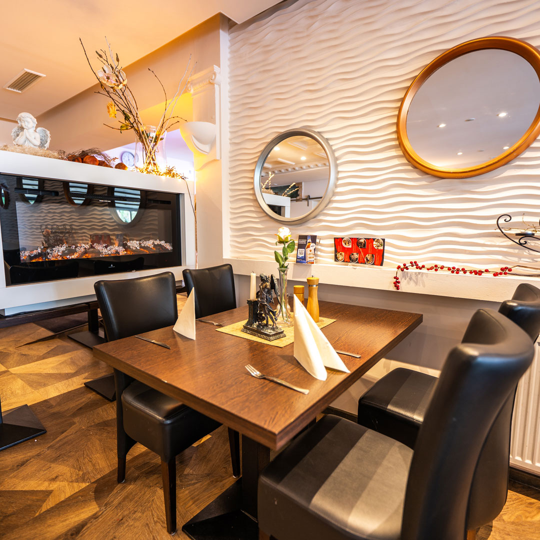 Holztisch für vier in einem Restaurant, gedeckt mit weißen Servietten, Kerze und Rose vor elektrischem Kamin und welliger Wand